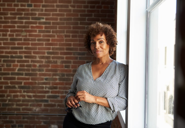 Woman leans against window with brick wall behind her