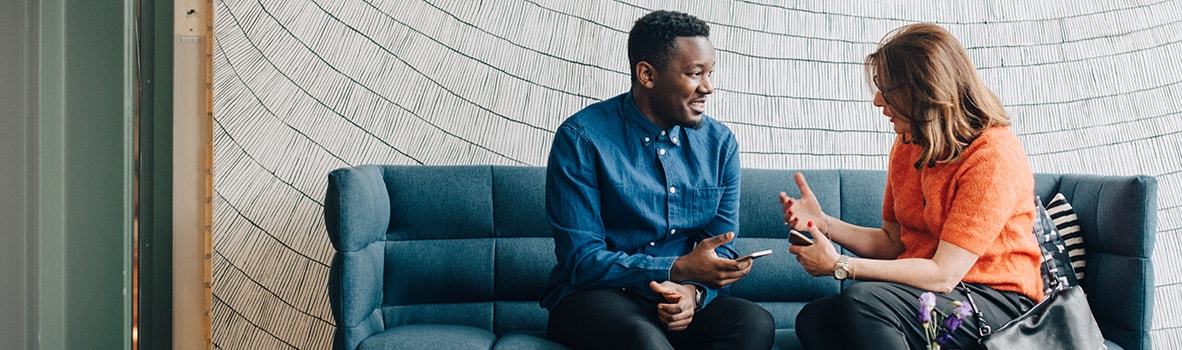 Businessman and woman taking while sitting on couch against wall in a conference room