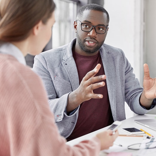 coworkers talk at desk with laptop on it