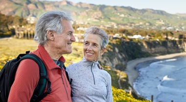Older couple smile as they stand near an oceanside cliff