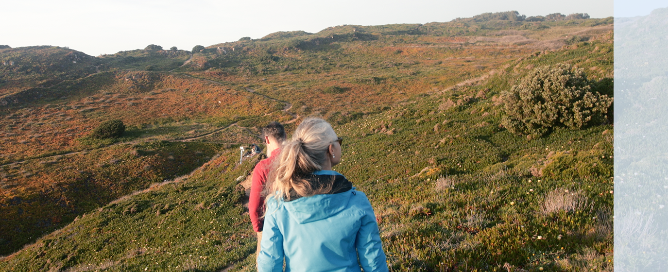 people walking on trail with expanse of field and hills ahead of them