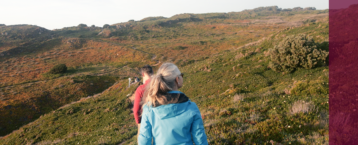 people walking on trail with expanse of field and hills ahead of them