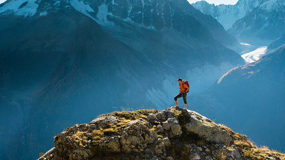 hiker standing atop mountain within mountain range