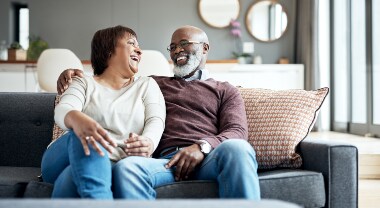 An older couple sits on couch and smiles at each other