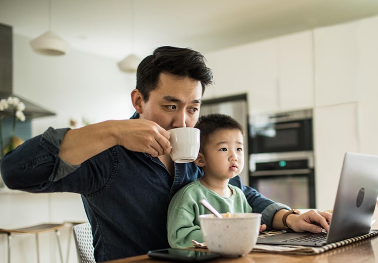 man works on laptop with toddler son on lap