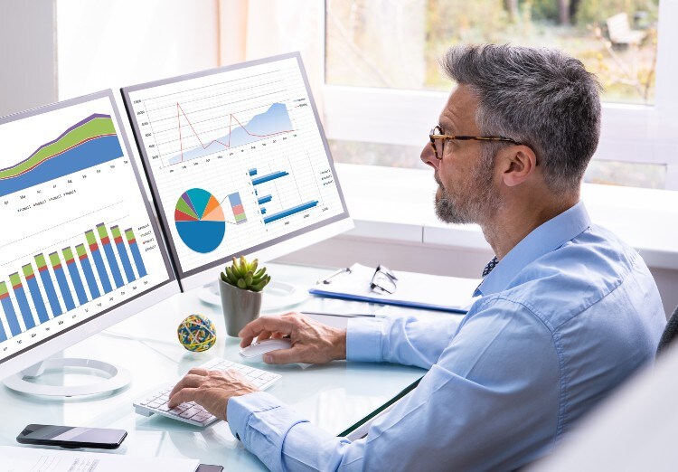 Man looking at graphs on desktop computer screens