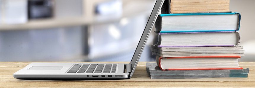 pile of books sit behind open laptop