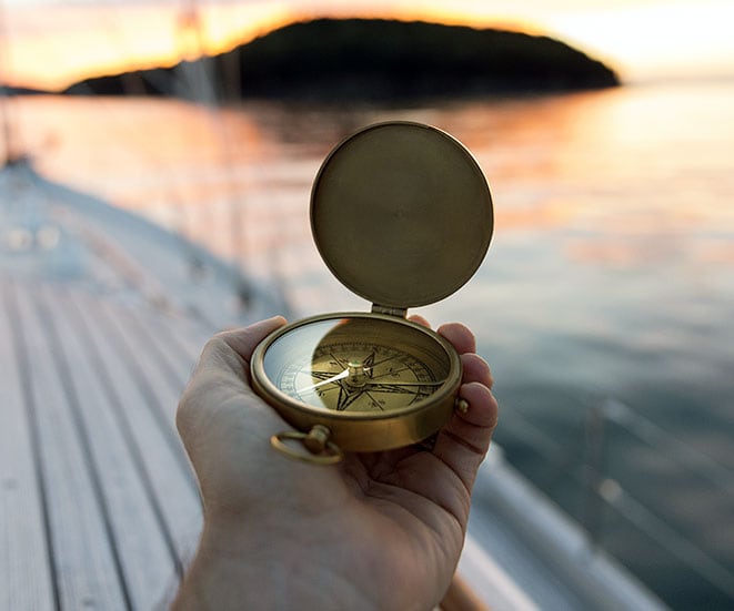 A hand holding a compass pointing out into the ocean.