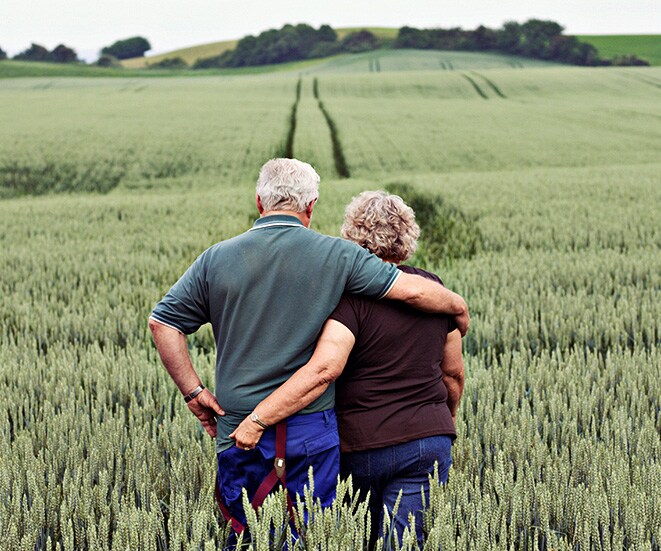 An older couple walking through high grass.