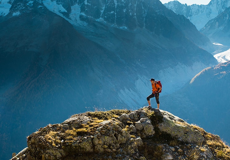 hiker on top of mountain with rest of mountain range in background