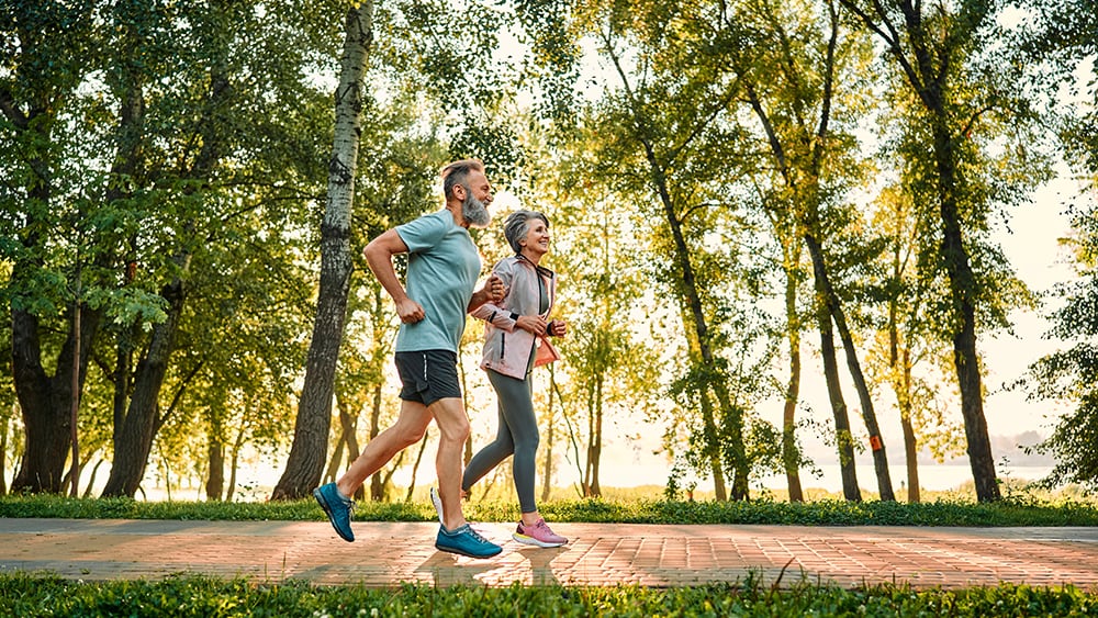 older couple jogs on path in wooded area