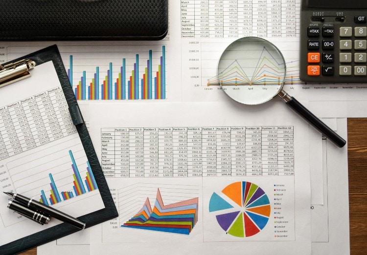 spreadsheets, magnifying glass, tablet, and calculator sit on desk