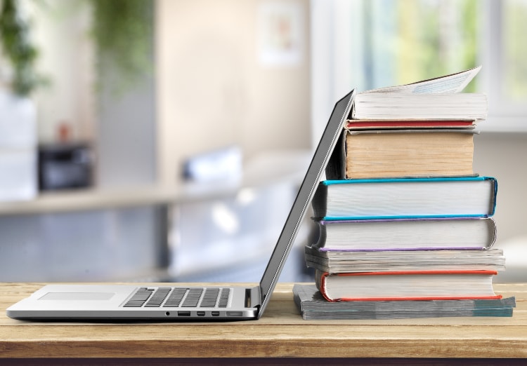 pile of books sit behind open laptop