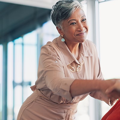 standing woman shakes hands with person seated across from her