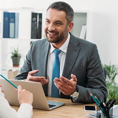 businessman sits behind desk and gestures with his hands