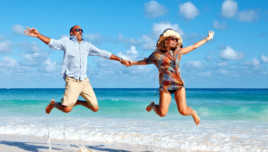 Couple on shoreline of beach jump into the air