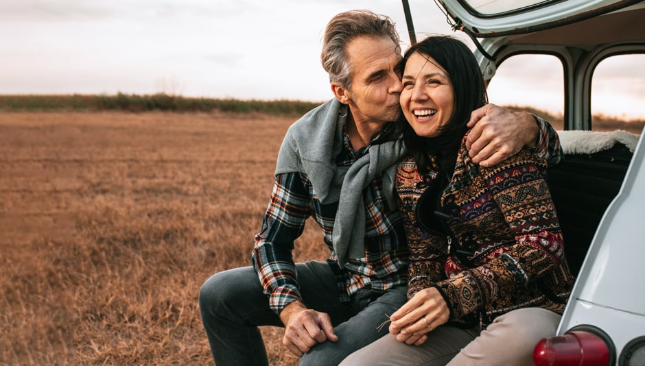 Couple sit in the open back of an SUV looking out into a field