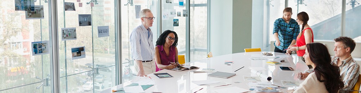 A diverse group of business colleagues talking around a large table filled with notes in conference room