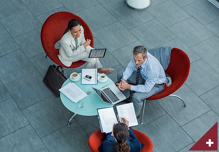 High angle view of 3 business people discussing strategy at coffee table in office