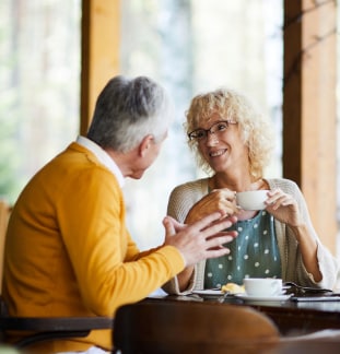 2 people sit at table and drink from mugs