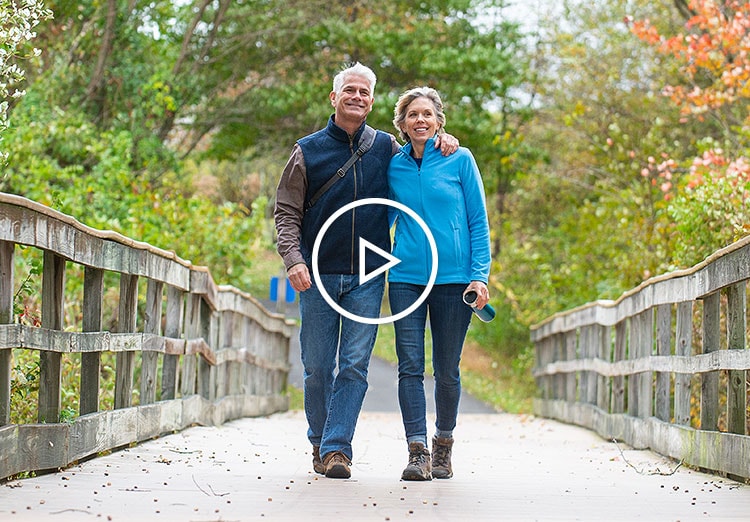 Man and woman walking shoulder to shoulder on a bridge in the woods