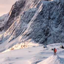 Lone mountaineer stands on snowy hill with mountains in the distance