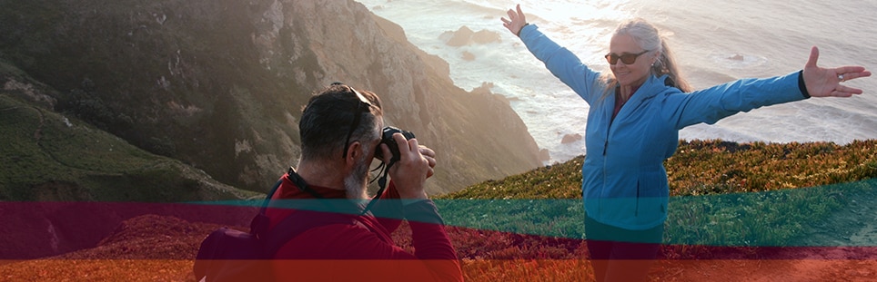 man takes photo of woman standing on cliff