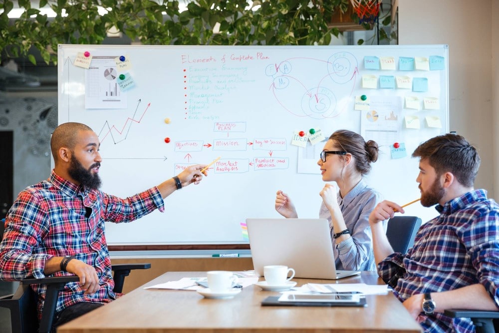 coworkers work at table with whiteboard in background