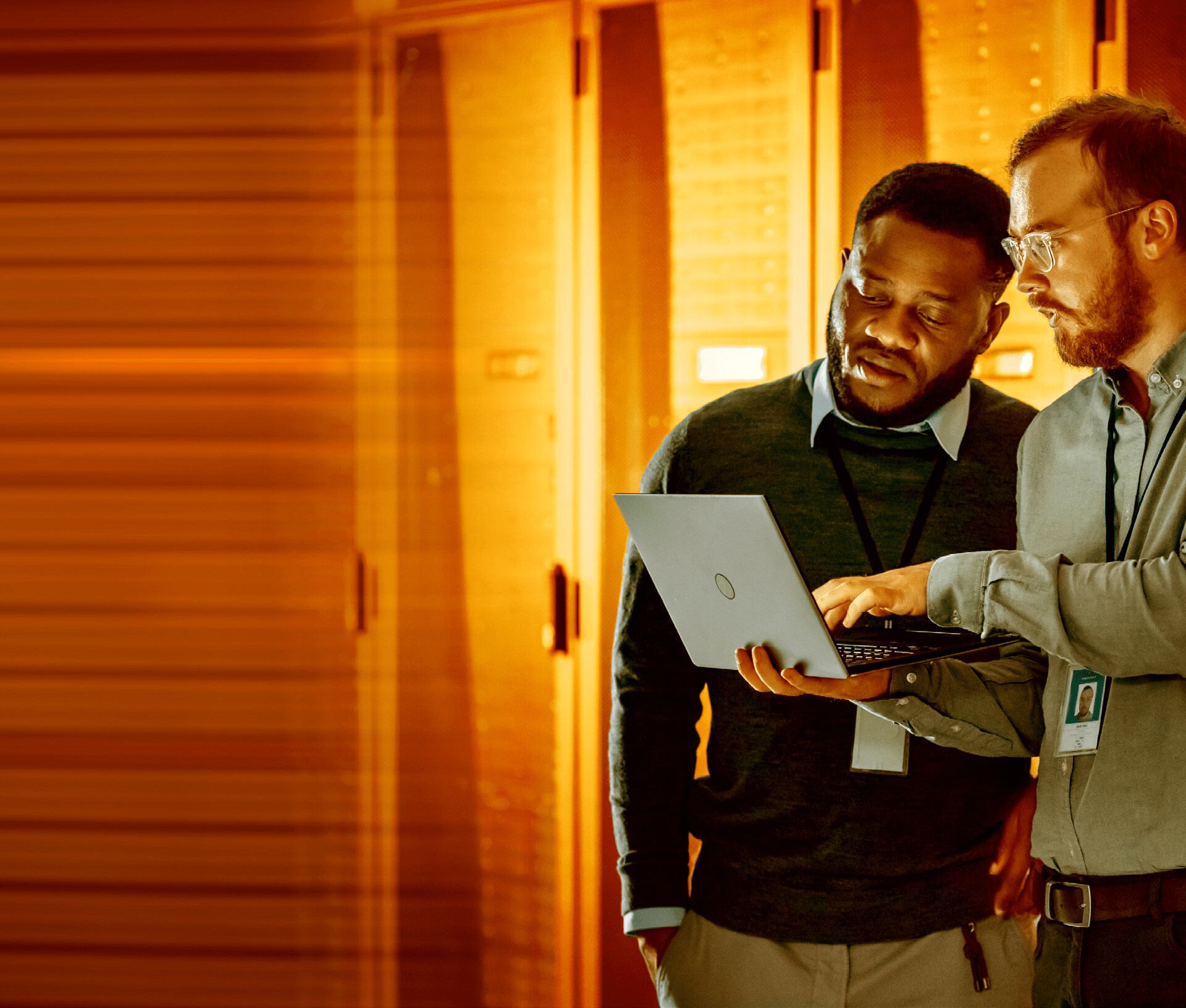 Two i t workers looking at a laptop in a server room