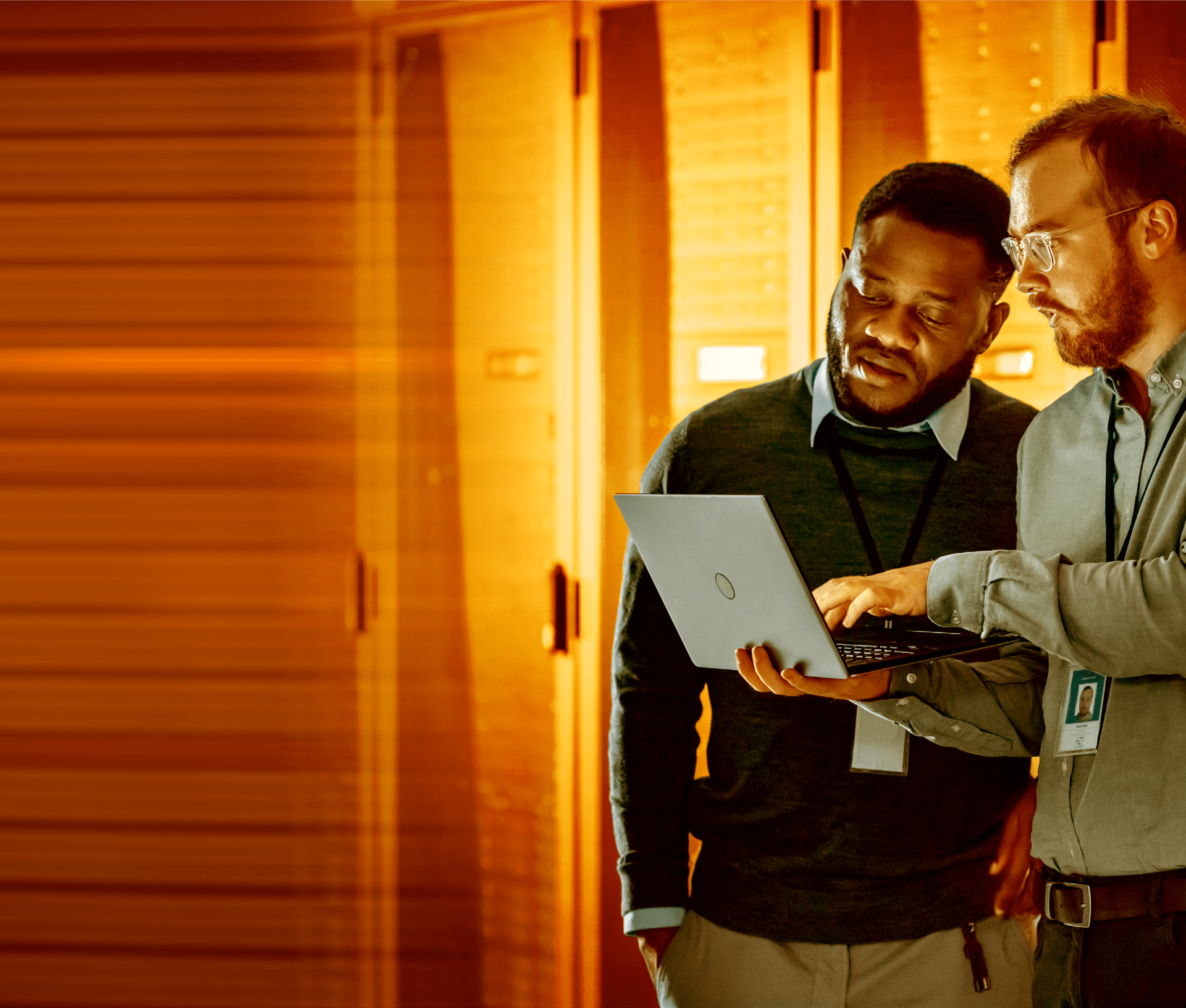 Two i t workers looking at a laptop in a server room