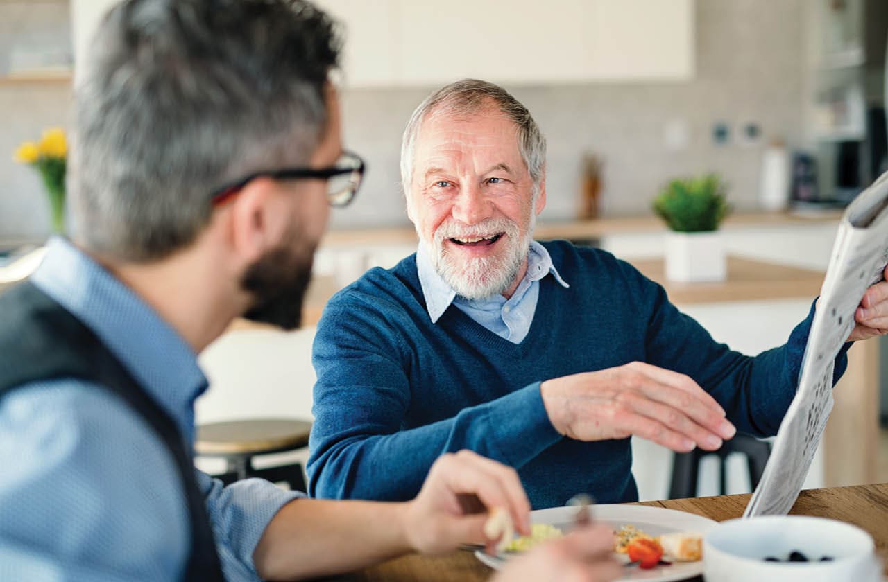 an elderly man and his son are eating breakfast together and talking