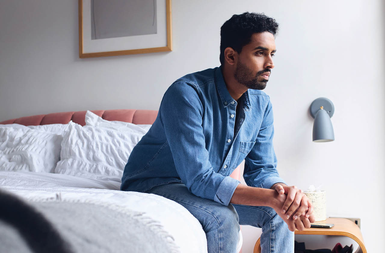 man sitting on the egde of a bed, and staring off into the distance
