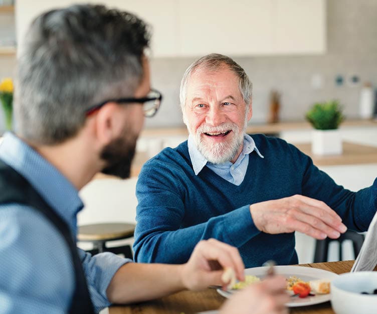 an elderly man and his son are eating breakfast together and talking