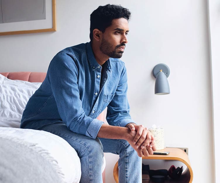man sitting on the egde of a bed, and staring off into the distance