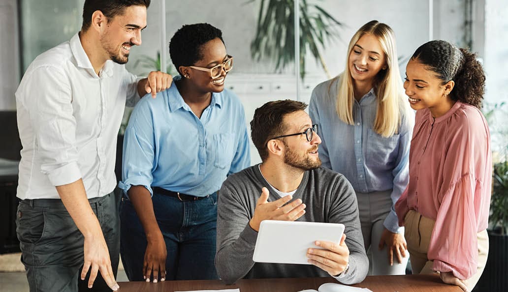 five coworkers having a meeting while looking at an electronic tablet