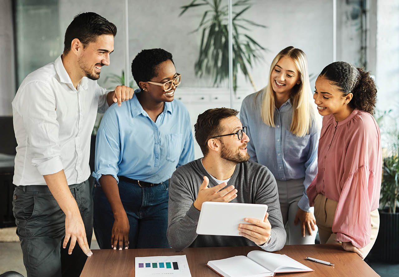 five coworkers having a meeting while looking at an electronic tablet