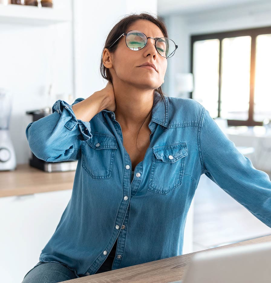woman working on laptop looking stressed. she is holding the back of her neck and stretching.