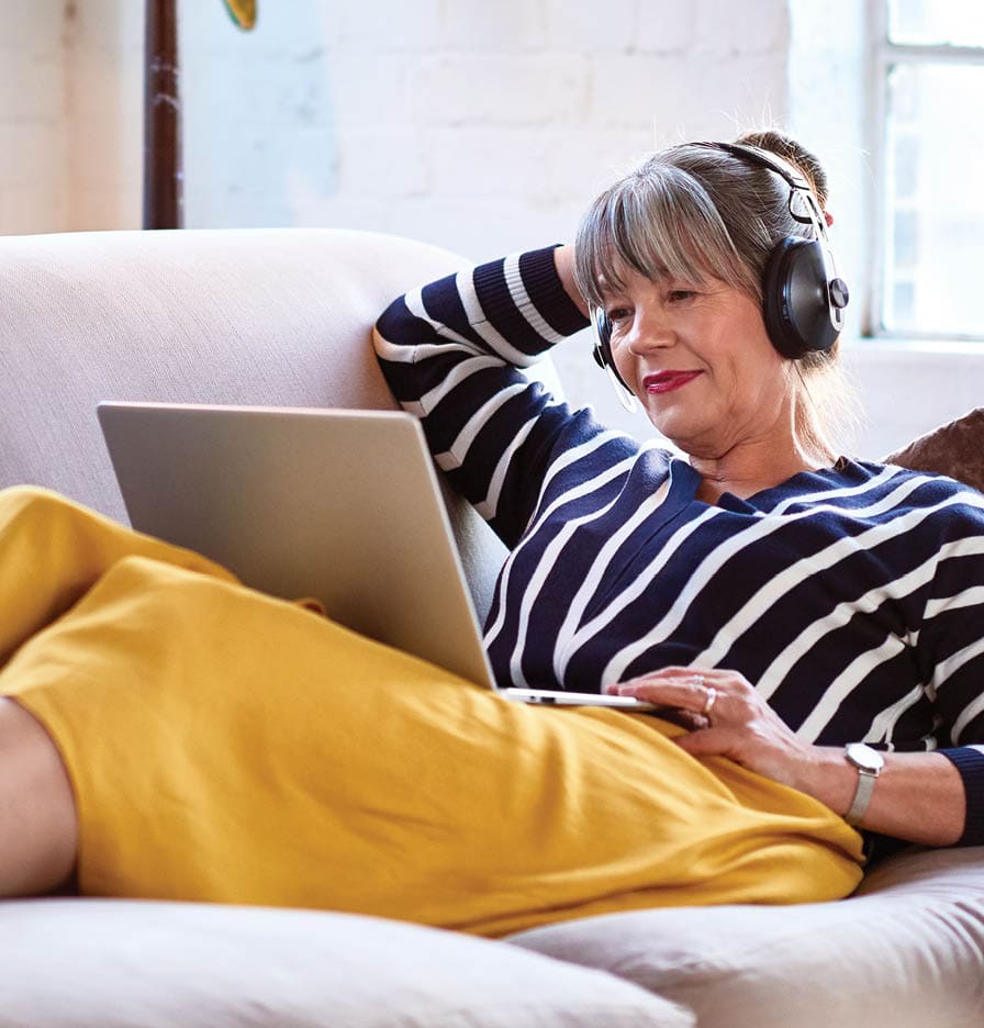 older woman on couch with a laptop. she has a prosthetic leg