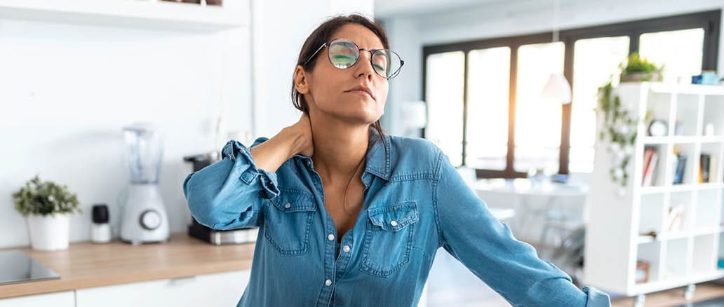 woman working on laptop looking stressed. she is holding the back of her neck and stretching.