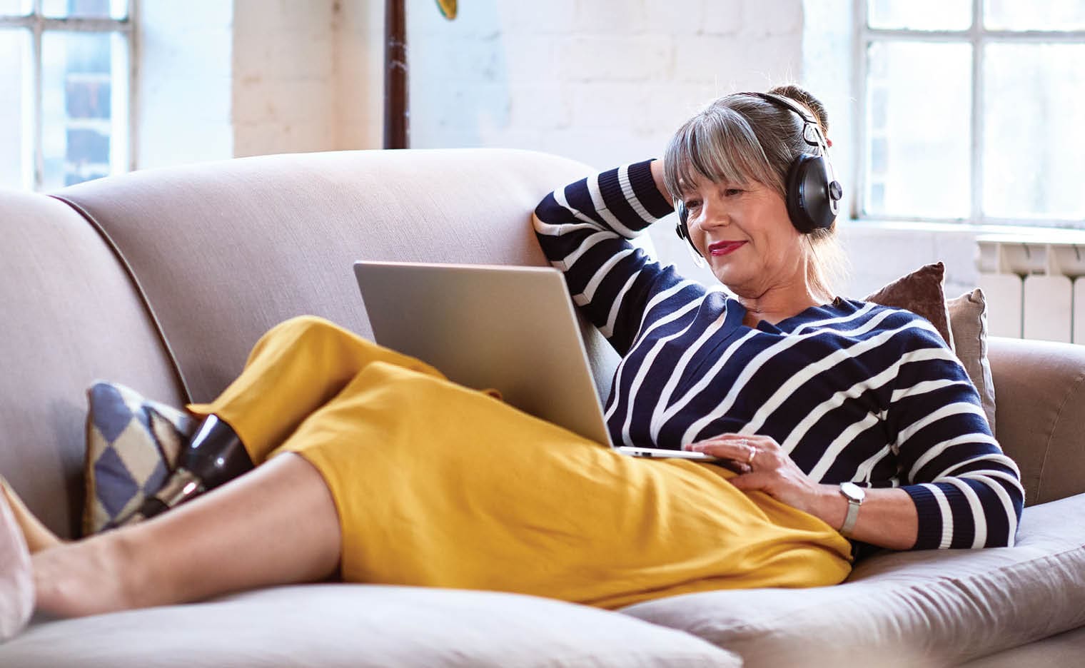 older woman on couch with a laptop. she has a prosthetic leg
