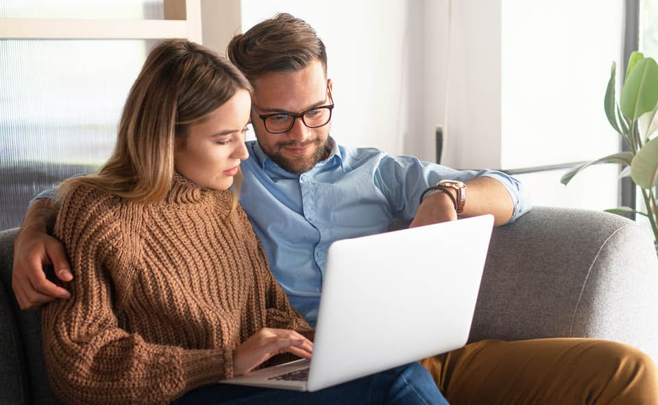 a couple is sitting on a couch and looking at a laptop together