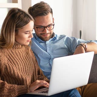a couple is sitting on a couch and looking at a laptop together
