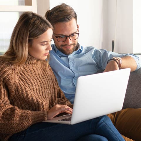 a couple is sitting on a couch and looking at a laptop together