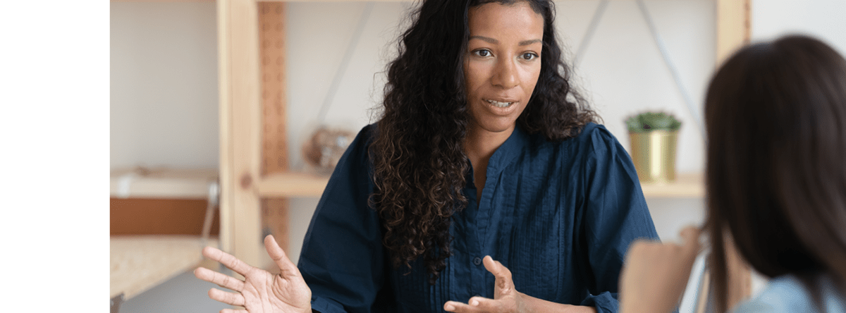 Two women are having a business meeting. One is talking and gesturing with her hands.