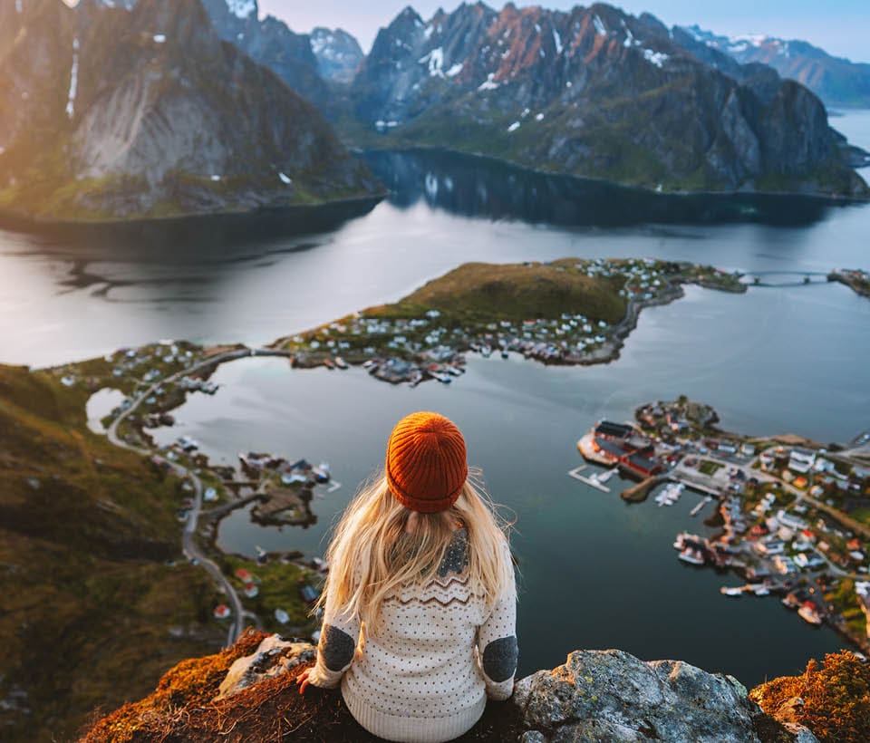 woman sitting on rocks, looking at mountains across the water