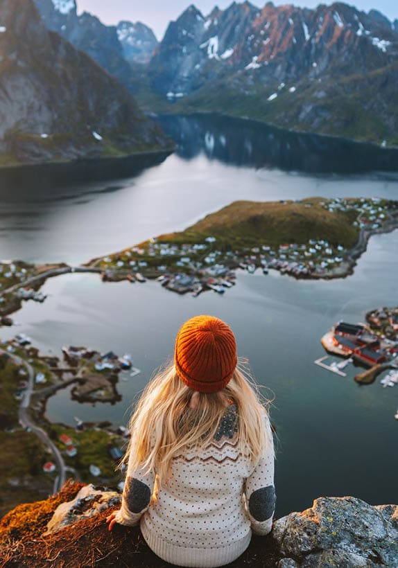 woman sitting on rocks, looking at mountains across the water