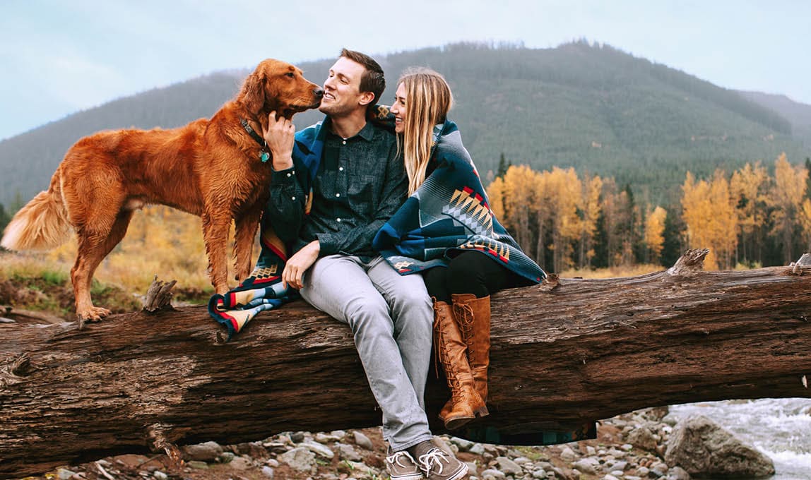 hiking couple with a dog sitting on a log in the mountains