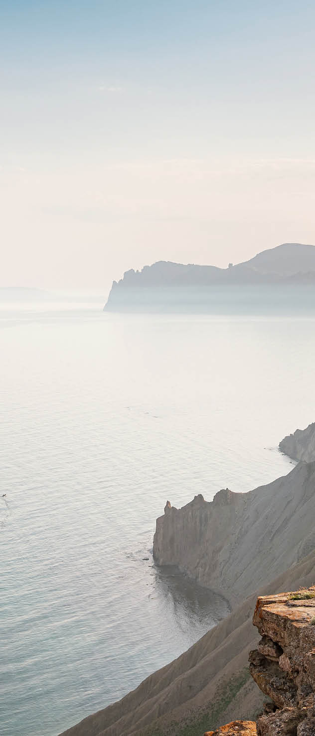 a hiker sits on mountaintop rocks looking out over vast water and mountains