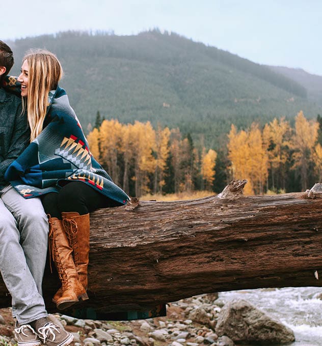 hiking couple with a dog sitting on a log in the mountains