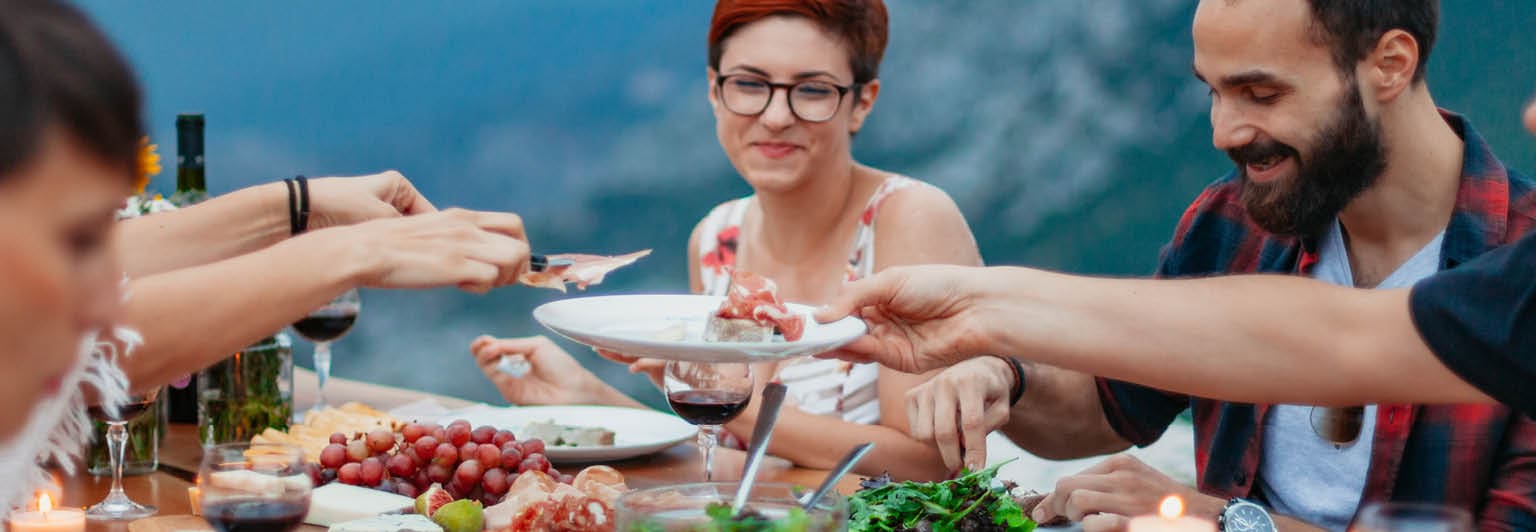 Friends and family gathered for picnic dinner for Thanksgiving. Festive young people celebrating life with red wine, grapes, cheese platter, and a selection of cold meats